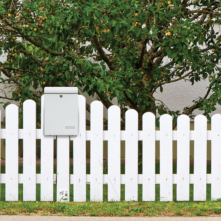 einzelner Briefkasten an weißem Zaun